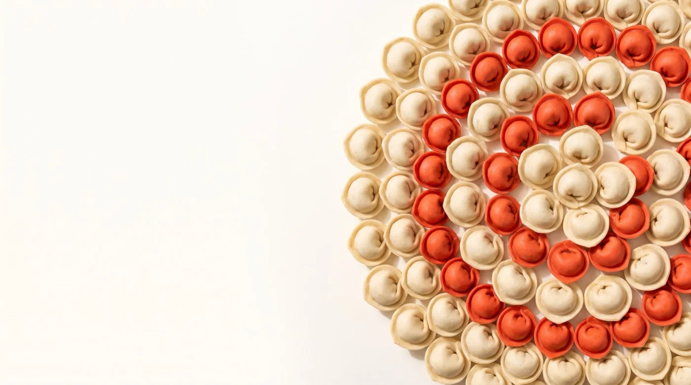 Handmade pelmeni arranged in a tomato-and-cream mandala, ready to freeze